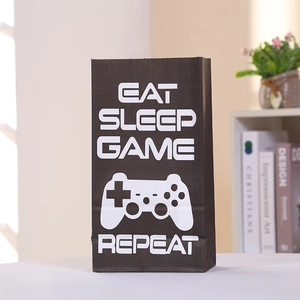 Détail d'un sac cadeau noir en kraft avec inscription Eat Sleep Game Repeat et manette