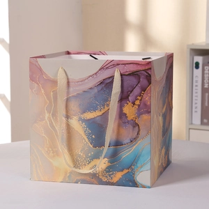 Elegant paper gift bag with purple fluid marble pattern and golden ribbon handles