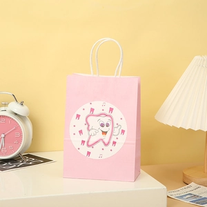 Close-up of pink gift paper bag with cartoon tooth motif and white twisted handles