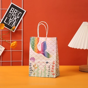 Detail of mermaid tail gift bag with colorful scales and white woven handles on a desk