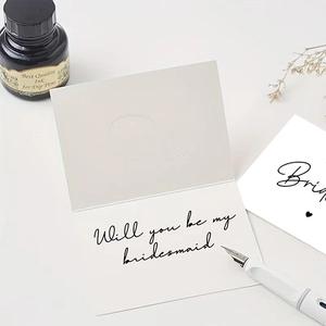 Elegant white folded Will You Be My Bridesmaid card set with calligraphy on white desk