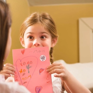 Girl holding pink card with Happy Mother's Day round stickers and heart pattern