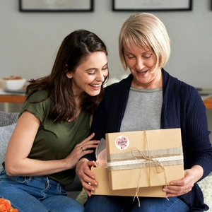 Close-up of Mother's Day gift box with heart sticker and ribbon held by a family