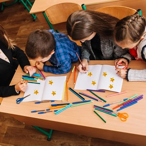 Children using gold star stickers and colorful pens for DIY craft in a classroom setting
