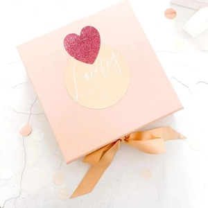 Detail of pink gift box with custom name sticker, red glitter heart and gold silk ribbon