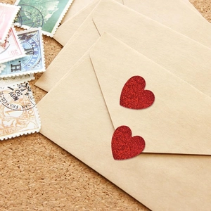 Detail of red glitter heart stickers on vintage kraft envelopes and cork board backdrop