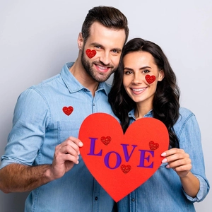 Close-up of red glitter heart stickers used as festive facial and clothing decoration