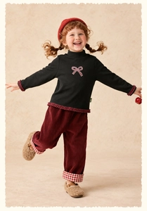Detail von schwarzem Mädchen-T-Shirt mit Schleife und bordeauxroter Cordhose im Set