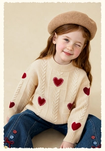 Detail of children's knit sweater featuring red heart patterns and cable knit texture