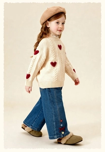 Close-up of girls' cable knit sweater with red heart patterns and denim bow jeans