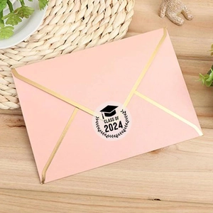 Pink graduation envelope with Class of 2024 gold foil sticker on wooden background