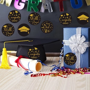 Detail of round black and gold graduation stickers with hats and scrolls on a gift box