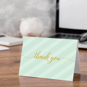 Elegant green striped thank you cards with gold foil text on a wooden desk setup