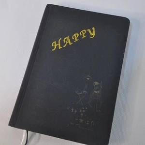 Detalle de cuaderno A5 negro con letras HAPPY en purpurina dorada y cinta blanca