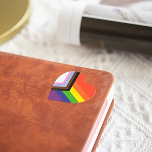 Square Progress Pride heart sticker on brown leather notebook with lace background