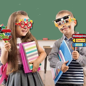 Children at school using graduation party photo props and colorful paper glasses
