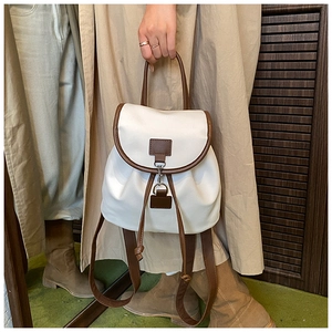 Detailed view of women's white nylon backpack with brown leather trim and metal lock closure