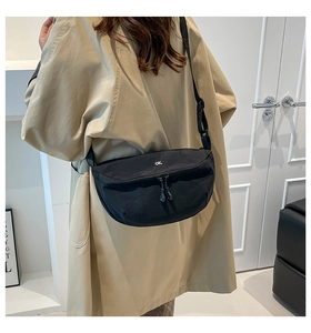 Detail of black crescent crossbody bag with white OK logo on model in khaki trench coat