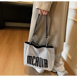 Detail of grey canvas tote bag featuring black embossed text and leather chain straps