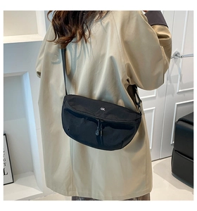 Detailed view of black crescent crossbody bag with white ok badge on khaki coat