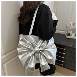 Detail of silver metallic tote bag featuring a large bow and glossy leather texture