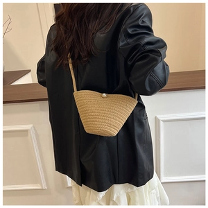 Detail of woven straw bucket bag featuring a large pearl clasp on the shoulder strap