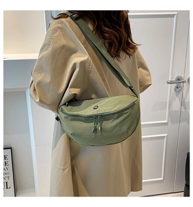 Close-up of grass green nylon crescent saddle bag with circular logo on a beige trench coat