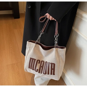 Detail of off-white canvas tote bag with brown leather handles and silver chain accents
