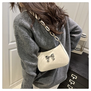 Detail of cream white underarm bag with silver metal bow and resin ring chain strap