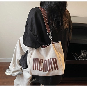 Rear view of a beige canvas tote bag with brown leather and silver chain straps