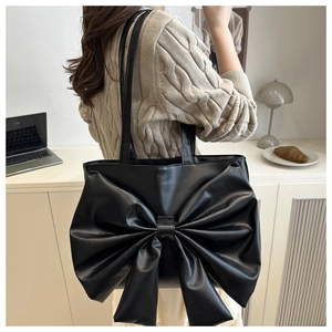 Side view of black faux leather tote bag with large bow and slim shoulder straps