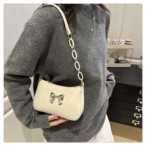 Detail of white crossbody bag featuring silver metal bow and leather chain strap