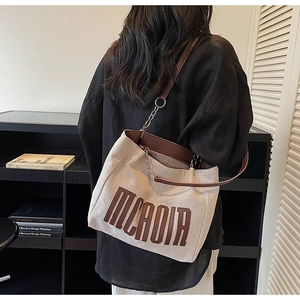 Detail of canvas tote bag with MCAOIR embroidery and leather handles with chain accents