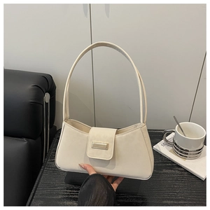 Sac sous le bras beige chic avec boucle métallique posé sur une table en bois