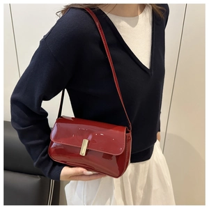 Detail of red patent leather shoulder bag with sleek gold bar metal lock closure