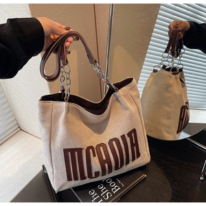 Detail of canvas tote bag featuring brown leather MCADIA letters and chain strap