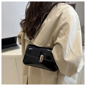 Close-up of black patent leather shoulder bag with a gold metal clasp on a trench coat