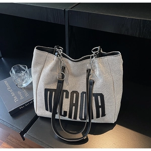 Detail of canvas tote bag with bold black letter embroidery and metal chain strap