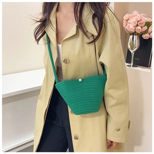 Detail of green knitted bucket bag with pearl clasp closure on beige coat background