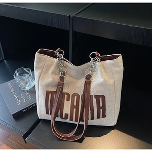 Detailed view of the beige canvas tote bag with brown leather handles and metal chain links