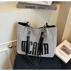 Detail of grey canvas tote bag with MCMA lettering and black leather chain straps