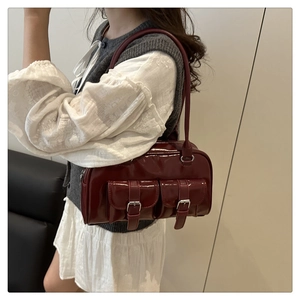 Detail of burgundy glossy leather shoulder bag with decorative buckle pockets on front