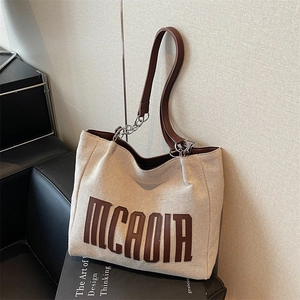 Large beige canvas tote bag with brown leather handles and metal chain decoration