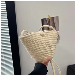 Detail of cream woven bucket bag featuring a large pearl clasp and textured fiber finish