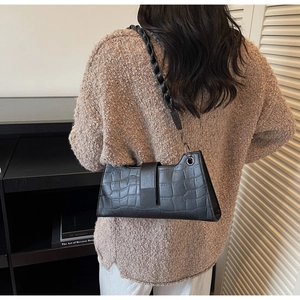 Detail of black faux crocodile leather baguette bag with woven strap on model shoulder