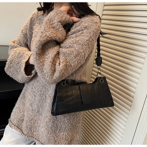 Detail of black faux crocodile leather shoulder bag with decorative woven strap and flap