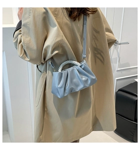 Detail of light blue pleated cloud bag with pearl handle worn over a khaki trench coat