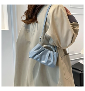 Close-up of light blue pleated cloud bag with pearl handle and long leather strap