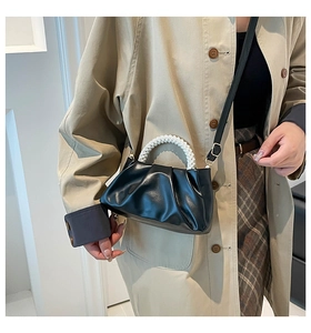 Detail of black pleated cloud bag with pearl handle worn with a beige trench coat