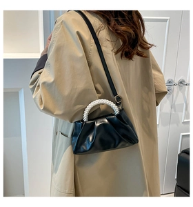 Fashionable black ruched cloud bag with pearl handle worn by a model in a trench coat